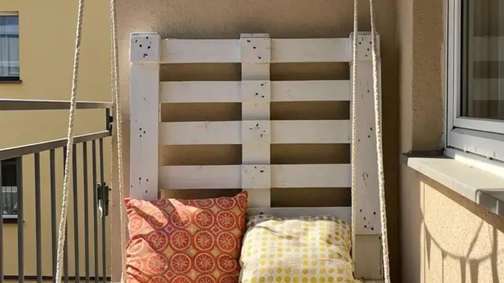 Compacte hangplek: een pallet schommel op een smal stadsbalkon met kussens.