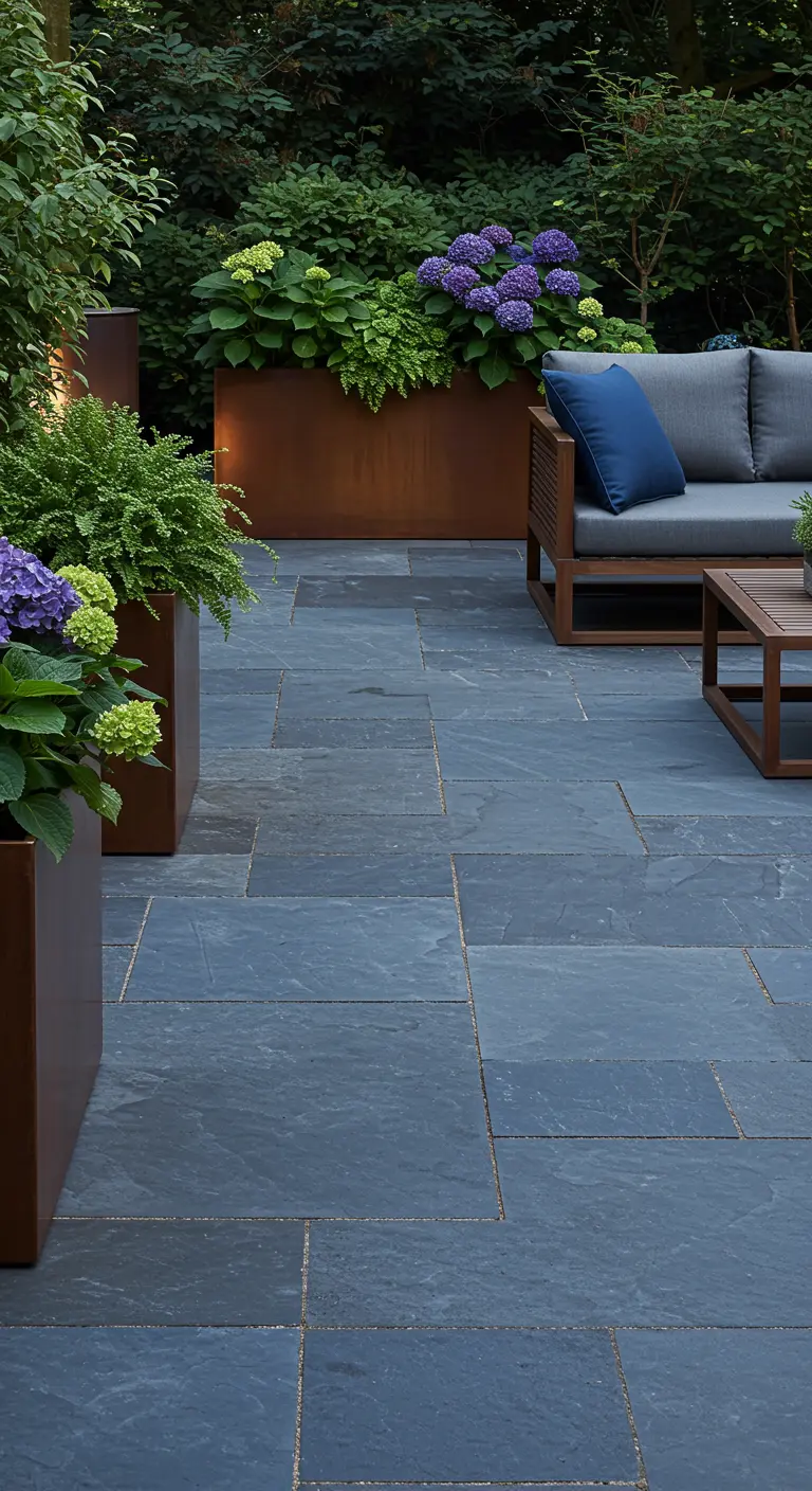 Donkerblauw leisteen terras met roestbruine cortenstaal plantenbakken gevuld met weelderige paarse en groene hortensia's.