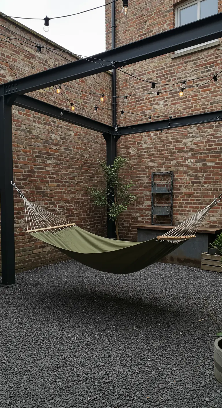 Olijfgroene hangmat opgehangen aan zwart metalen frame op een binnenplaats met gravel en bakstenen muur.