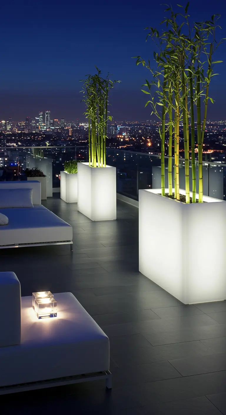 Hoge witte plantenbakken met ingebouwde verlichting en bamboe op modern dakterras bij nacht.