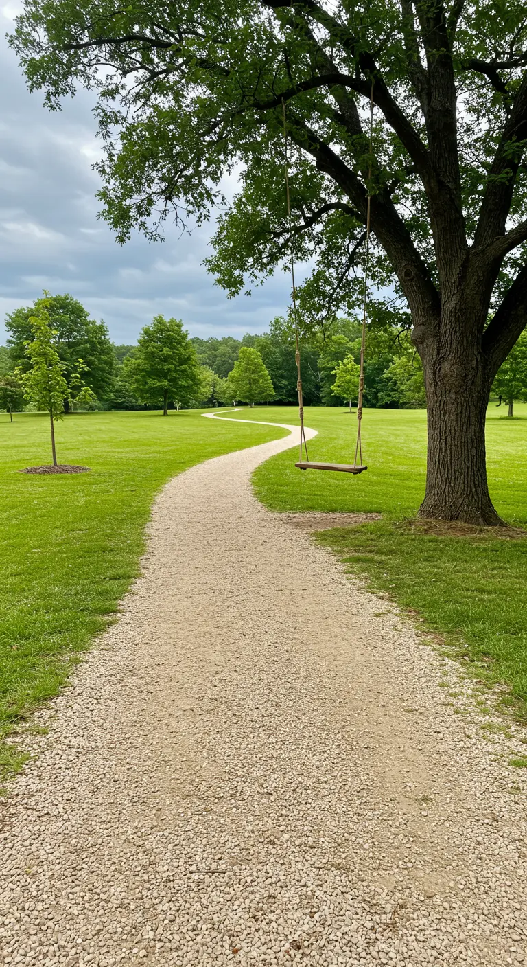 Boomstam-schommel aan boom langs een kronkelend grindpad door een groen grasveld.