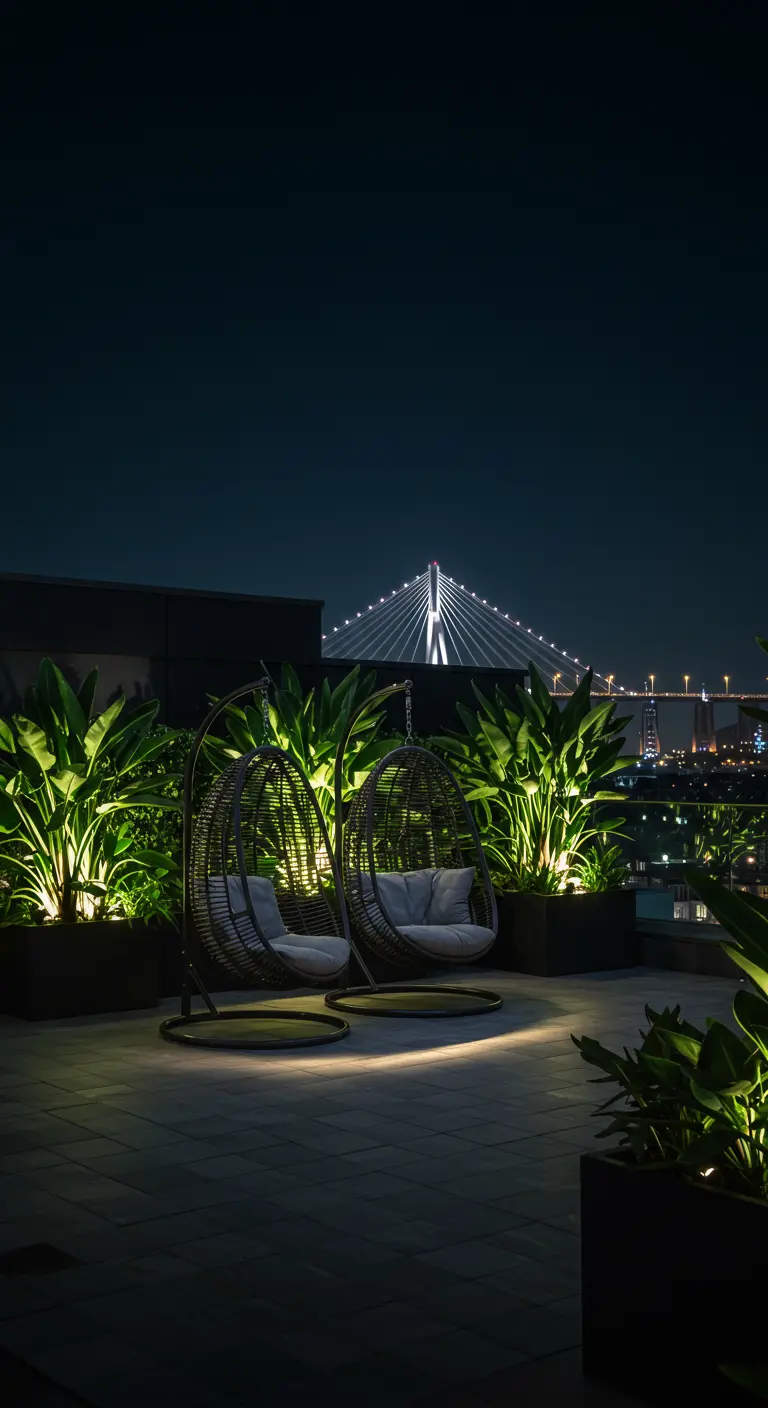Twee donkere rotan hangstoelen op een dakterras bij nacht, sfeervol verlicht door spotjes op de planten.