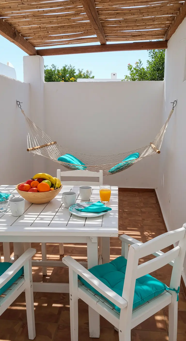 Balkon met witte eettafel, stoelen met turquoise kussens en een hangmat.