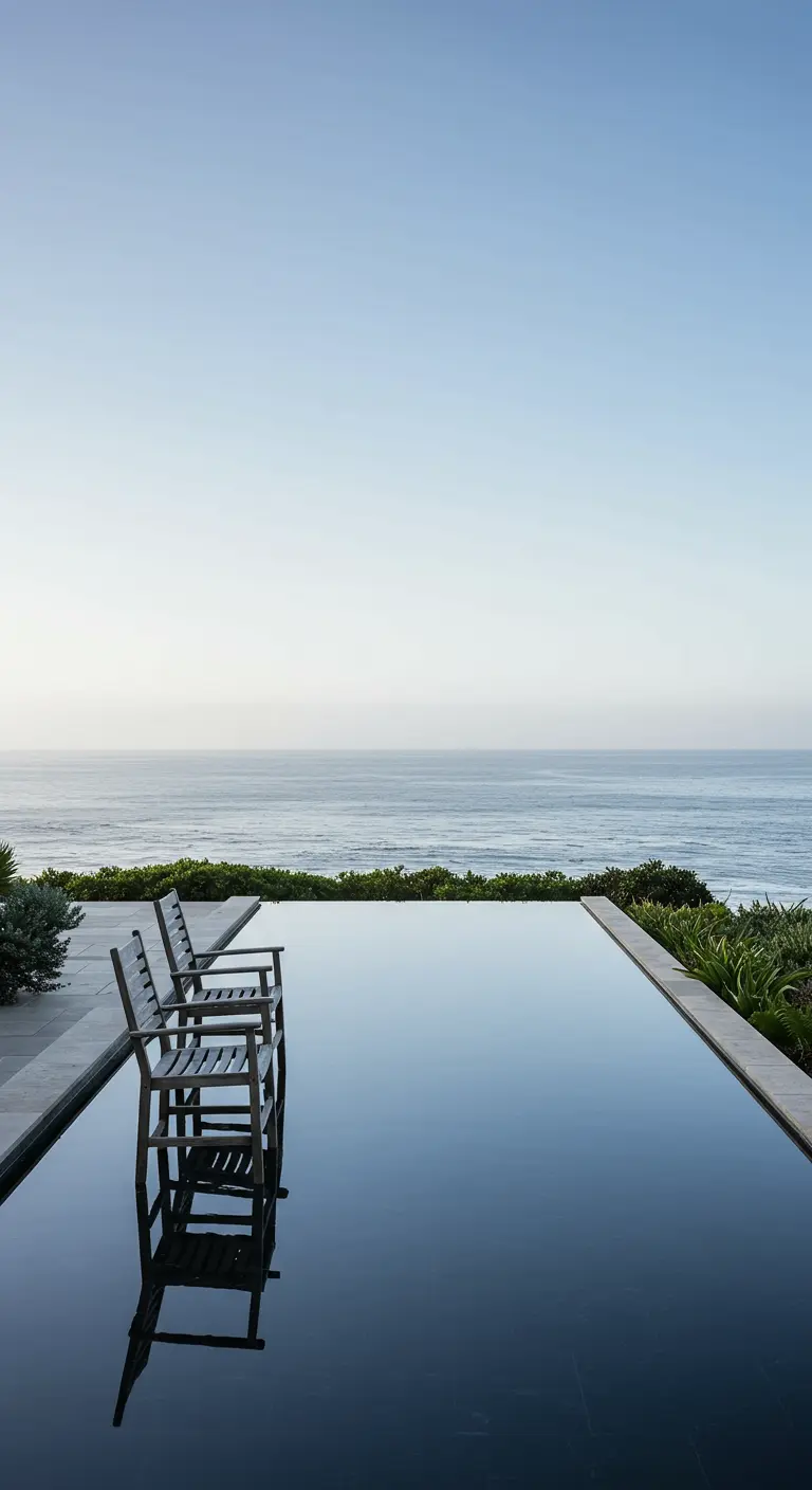 Donkere infinity pool die de lucht reflecteert, met stoelen en uitzicht op zee.