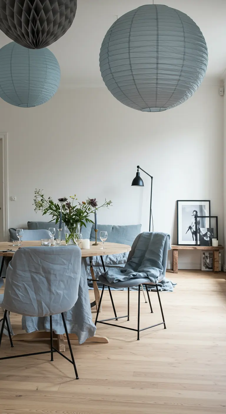 Minimalistische eetkamer met grijsblauwe lampions en linnen stoelhoezen in dezelfde kleur.