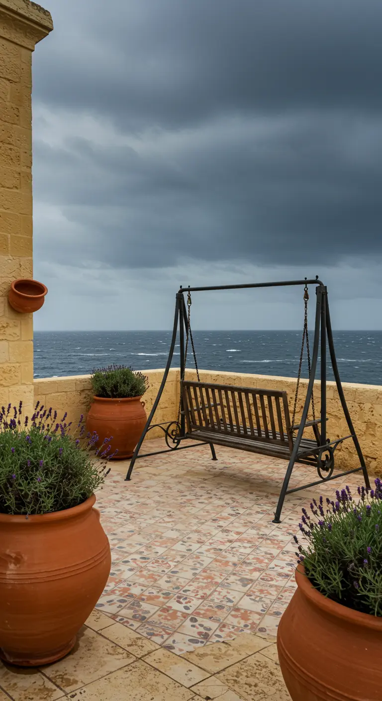 Zwarte metalen schommelbank op een betegeld balkon met uitzicht op een stormachtige zee.