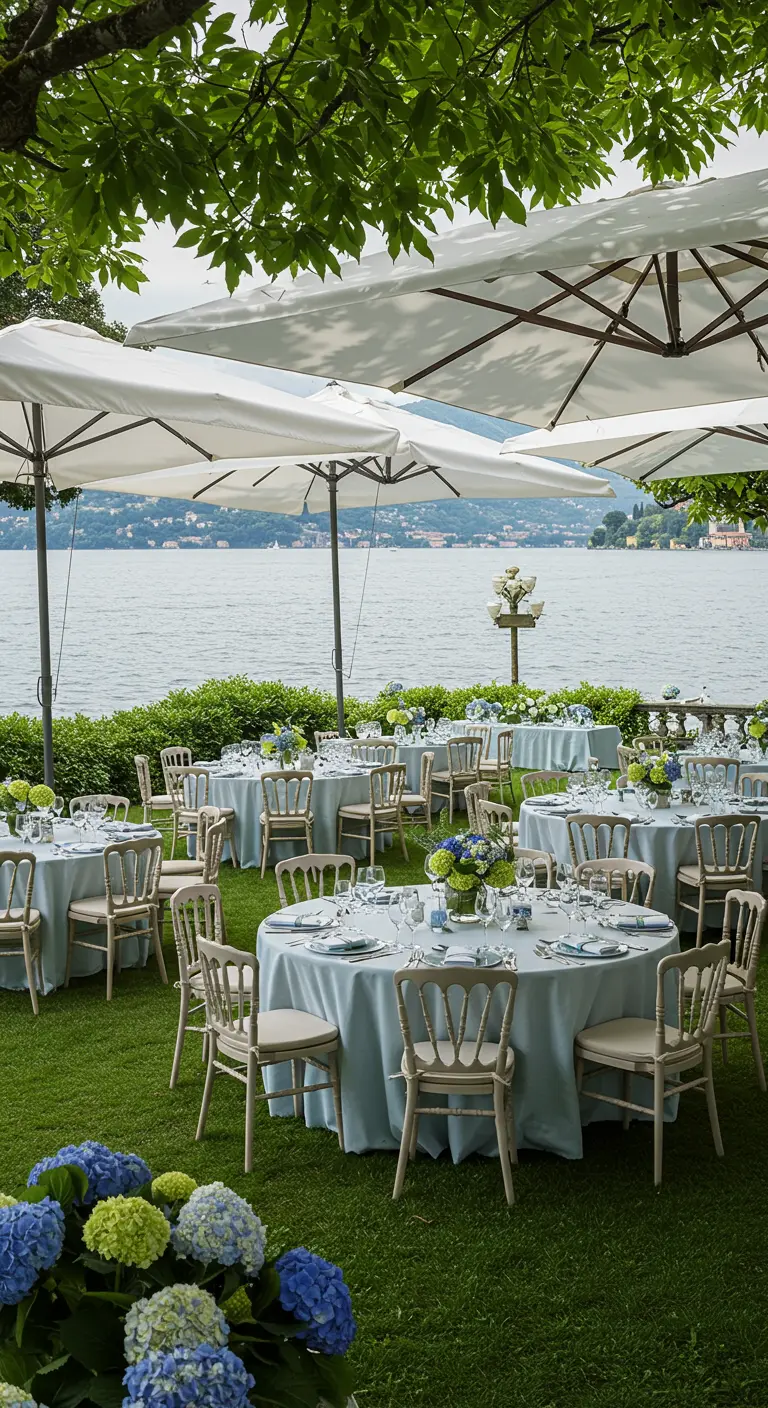 Tafels aan een meer met lichtblauwe kleden en blauwe hortensia's.